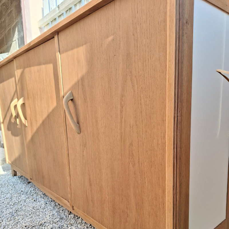 Vue de coté du meuble : détail des portes en chêne aux reflets miel, et sur les poignées épurées. Vue de coté du meuble : détail des portes en chêne aux reflets miel, et sur les poignées épurées.