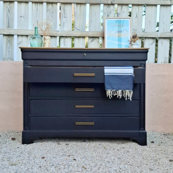 Commode ancienne upcyclée en noir et poignées cuivrées. Vue de face avec mise en ambiance : plaid et décorations diverses